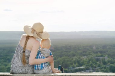 Anne ve oğlu yeşil orman ve villag uzak arka plan üzerinde oturuyor. Arkadan Görünüm