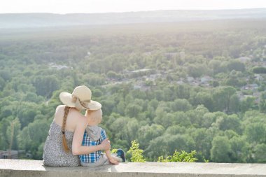 Anne ve oğlu yeşil orman ve köy uzakta arka plan üzerinde oturuyor. Arkadan Görünüm