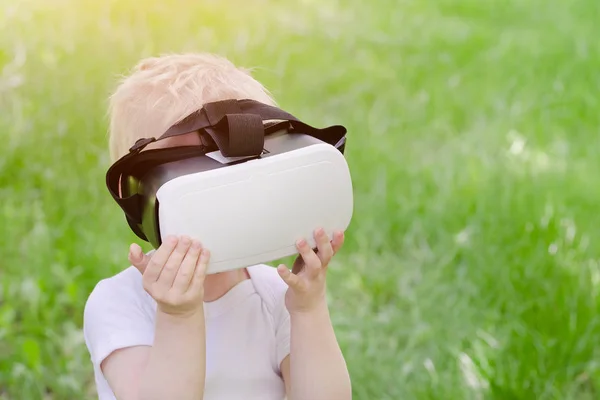 Niño en un casco de realidad virtual sobre un fondo de hierba verde —  Fotos de Stock