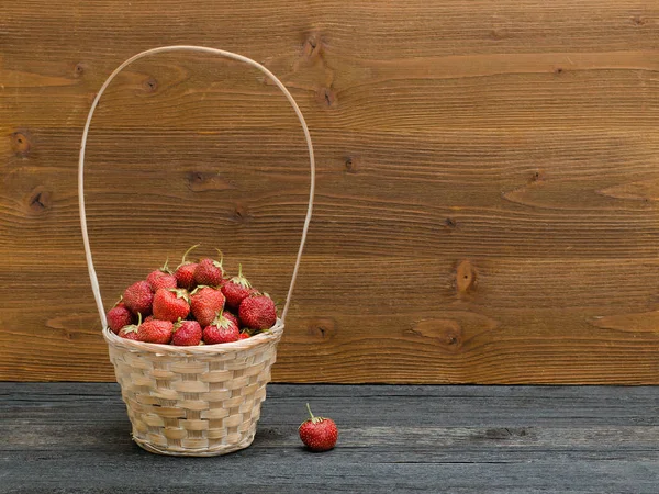 Cesta de fresas maduras sobre una mesa negra, fondo de madera . — Foto de Stock