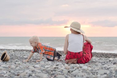 Anne ve oğlu çakıl plajı üzerinde oynamak. Günbatımı zamanı. Arkadan Görünüm