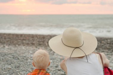 Anne ve oğlu çakıl plajı üzerinde bekletin. Günbatımı zamanı. Arkadan Görünüm
