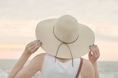 Şapkalı Kız deniz kenarında oturur. Arkadan Görünüm. Yakın çekim