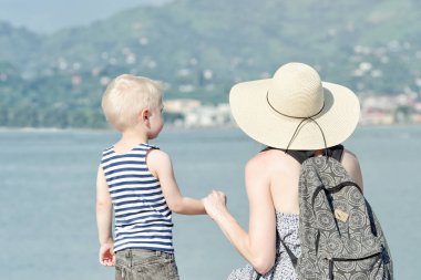 Anne ve oğlu deniz arka plan üzerinde iskelede. Şehir ve dağ uzakta. Arkadan Görünüm