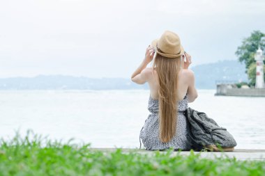 Güzel kız iskelede oturuyordu. Deniz ve deniz feneri küçük mesafe. Arkadan Görünüm