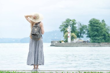 Deniz kenarındaki iskelede bir sırt çantası konumu olan şapkalı kız.