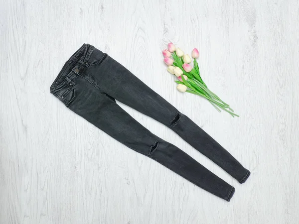 Modekonzept. graue zerrissene Jeans und rosa Tulpen. Holz Hintergrund — Stockfoto