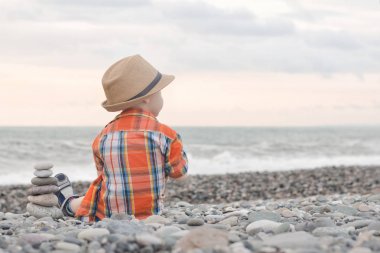 Şapkalı küçük çocuk oturup bir çakıl plajı