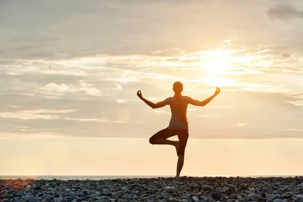 Meisje op zonsondergang praktizerende yoga bij de kust, achteraanzicht — Stockfoto