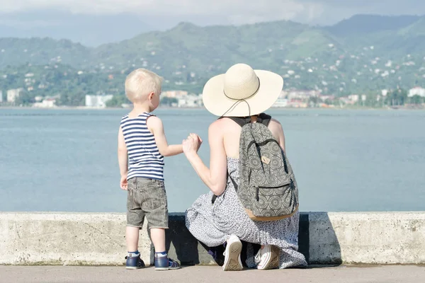 Anne ve oğlu deniz arka plan üzerinde iskelede. Şehir ve dağ uzakta. Arkadan Görünüm