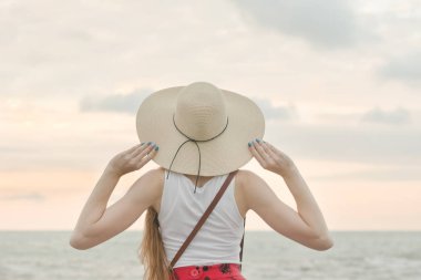 Şapkalı kız ayakta deniz, gün batımı. Arkadan Görünüm