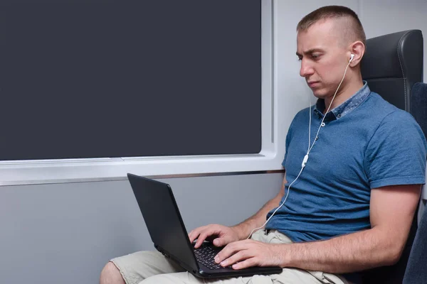 Young man working behind a laptop sitting in a train chair