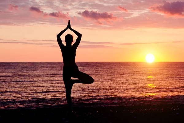 Vrouw bij zonsondergang praktizerende yoga. Kust, silhouet — Stockfoto