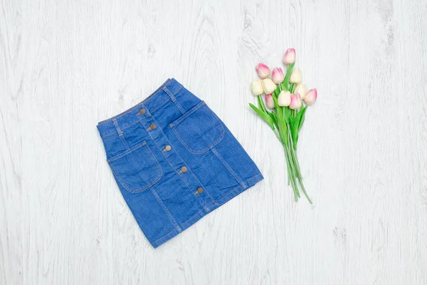 Fashion concept. Blue denim skirt and pink tulips. Wood background