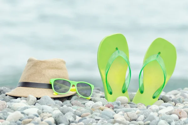 Капелюх, окуляри та фліп-флоп на гальковому пляжі. Море на задньому плані — стокове фото