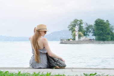 Güzel kız iskelede oturuyordu. Deniz ve deniz feneri küçük