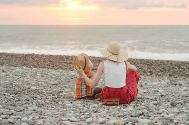 Anne ve oğlu çakıl plajı üzerinde oynamak. Günbatımı zamanı. Arkadan Görünüm
