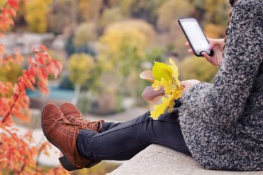 Kız bir telefon ile bir tepe üzerinde oturur, onun elinde sarı yapraklar.