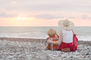 Anne ve oğlu sahilde oturan ve gün batımı hayranım. Arkadan Görünüm