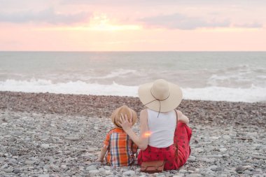 Anne ve oğlu çakıl plajı üzerinde bekletin. Günbatımı zamanı. Arkadan Görünüm