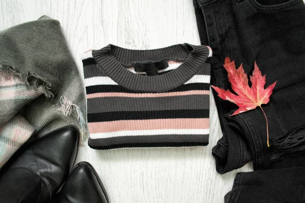 Camisola listrada, jeans pretos, botas e folha de bordo vermelho — Fotografia de Stock