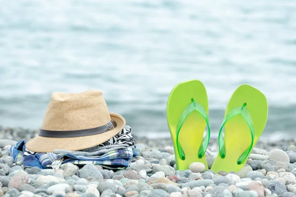 Chapéu, roupas e chinelos na praia de seixos. Mar ao fundo — Fotografia de Stock
