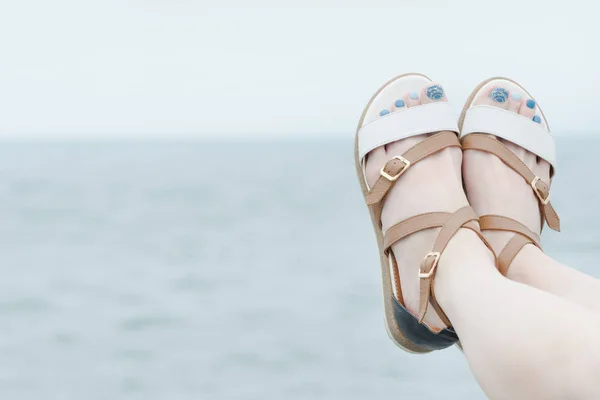 Pies femeninos en sandalias con manicura sobre fondo de mar — Foto de Stock