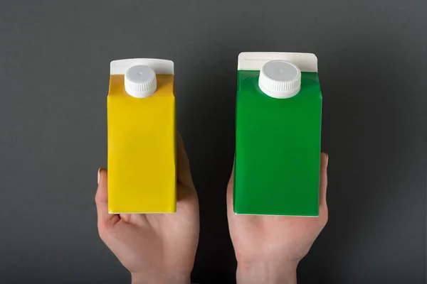 Caja de cartón amarillo y verde o envase de tetra en manos femeninas. Fondo negro —  Fotos de Stock