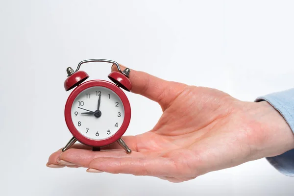 Reloj despertador rojo en una mano femenina sobre un fondo blanco — Foto de Stock