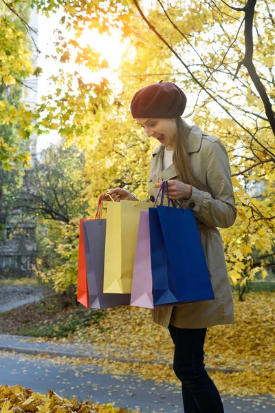 Překvapená mladá žena shopaholic s barevnými taškami. Podzimní listy na pozadí — Stock fotografie