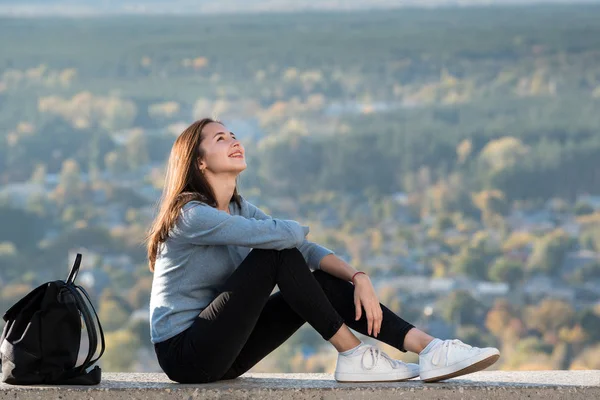 Smiling pretty girl sitting on a hill. Forest in the distance. sunny day — Stock Photo, Image