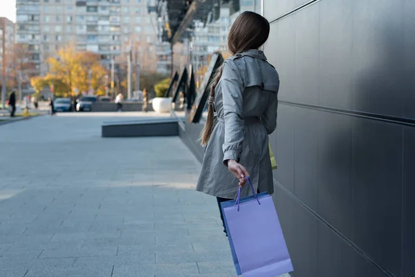 Mujer joven con bolsas de colores en la calle. Centro comercial en el fondo —  Fotos de Stock