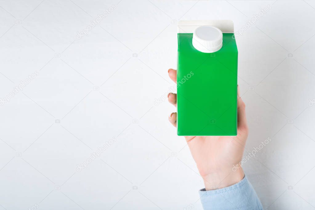 Green carton box or packaging of tetra pack with a cap in a female hand. White background