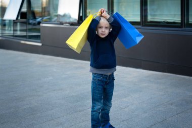 Alışveriş torbaları olan yorgun sarışın çocuk. Arkaplanda alışveriş merkezi