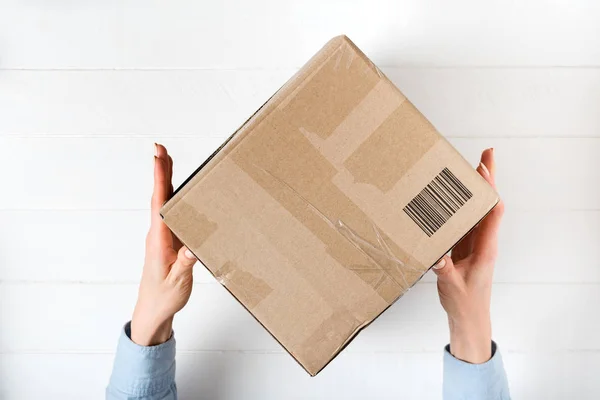 Square cardboard box with a barcode in female hands. Top view, w