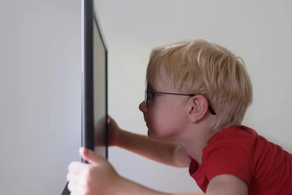 Ragazzo biondo con gli occhiali siede il naso sepolto in un monitor. Internet e asilo nido — Foto Stock