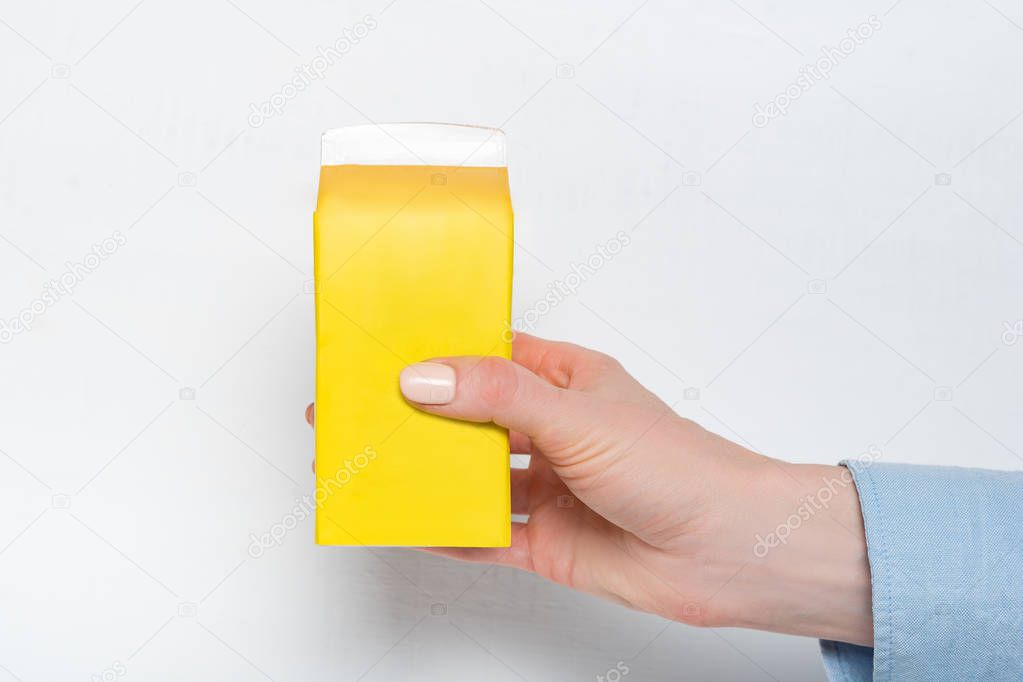 Yellow carton box or packaging of tetra pack in a female hand. White background