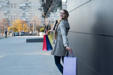Alışveriş merkezinin yakınında renkli çantaları olan mutlu genç bir kadın. Sokakta yürürken.