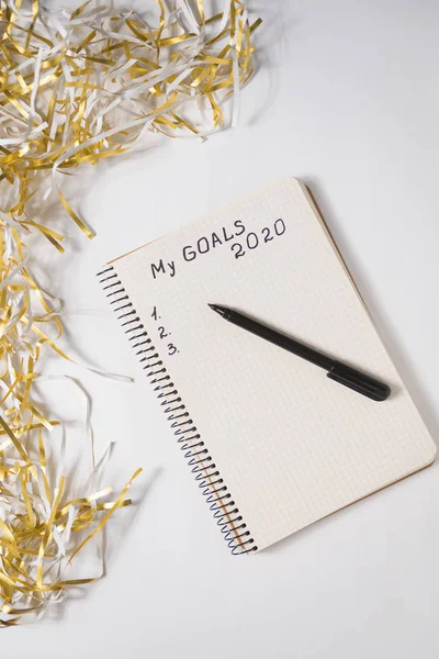 Phrase My Goals 2020 in a notebook, pen. Tinsel on white background