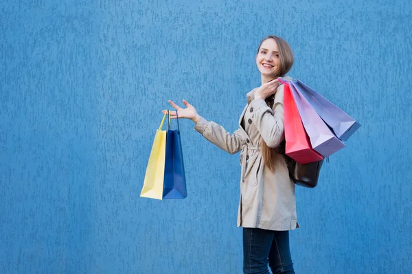 Szczęśliwa młoda kobieta zakupoholiczka z kolorowymi torbami. Niebieska ściana ulicy na tle — Zdjęcie stockowe