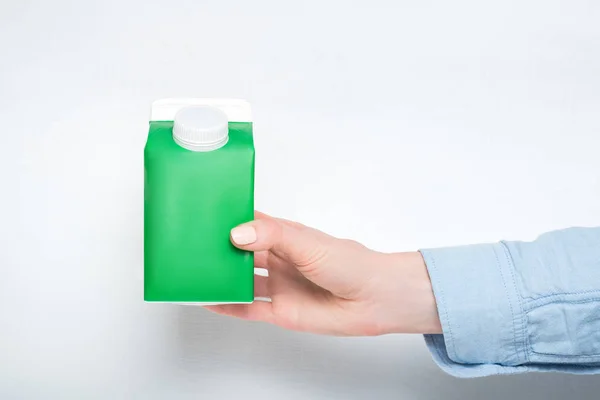 Boîte en carton vert ou emballage en tétra avec un capuchon dans une main féminine. Fond blanc — Photo