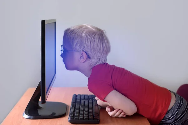 Niño rubio con gafas se sienta con la nariz enterrada en un monitor. Internet y preescolar — Foto de Stock