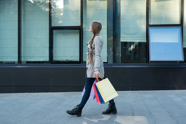 Mujer joven con bolsas de colores caminando por la calle. Centro comercial en el fondo —  Fotos de Stock