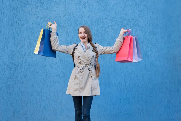 Vrolijke jonge vrouw shopaholic met kleurrijke tassen. Blauwe straatmuur op achtergrond — Stockfoto