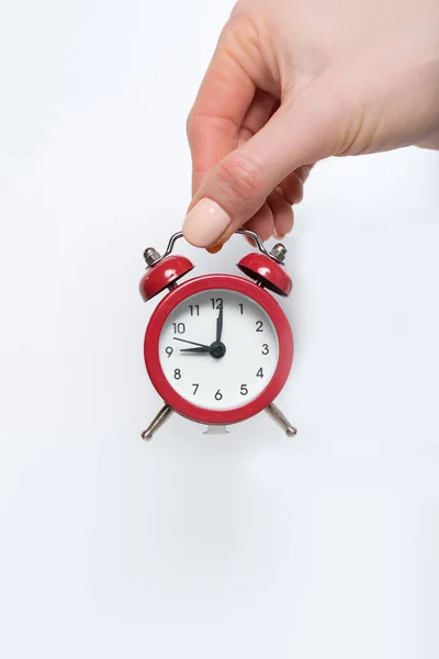Relógio de alarme vermelho em uma mão feminina em um fundo branco — Fotografia de Stock