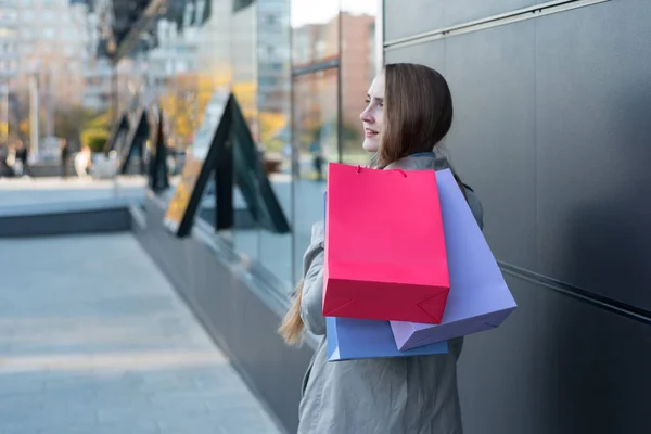 Mujer joven con bolsas de colores en la calle. Centro comercial en el fondo —  Fotos de Stock