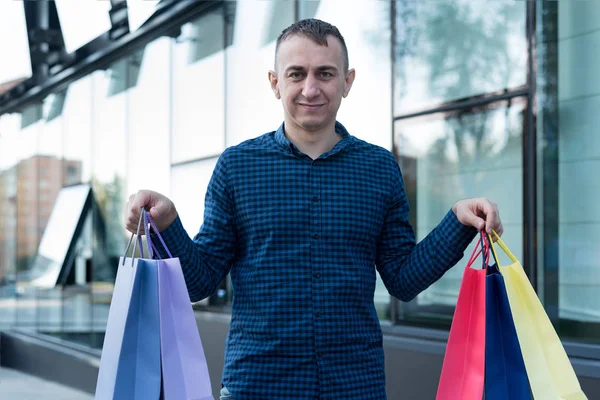 Sokakta renkli alışveriş torbaları taşıyan genç bir adam. Arkaplanda alışveriş merkezi — Stok fotoğraf