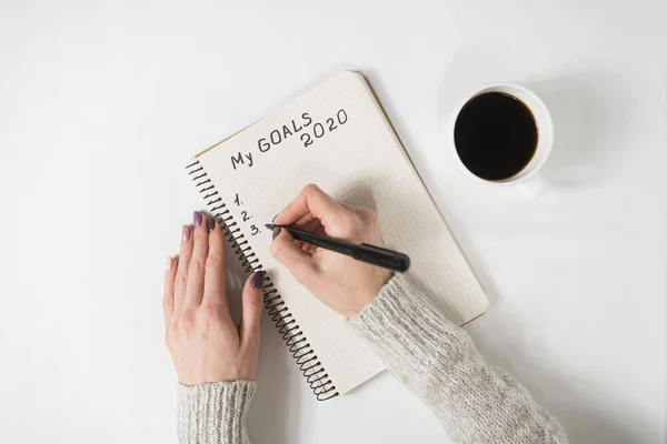 Frauenhände schreiben meine Ziele 2020 in ein Notizbuch. Kaffeebecher auf dem Tisch, Draufsicht — Stockfoto