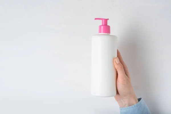 Біла косметична пластикова пляшка з насосом у жіночій руці. Білий фон — стокове фото
