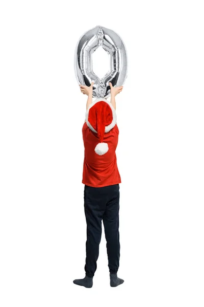 Мальчик в шляпе Санты держит серебряную надувную цифру ноль. Вид сзади. Изолированный на белом фоне . — стоковое фото